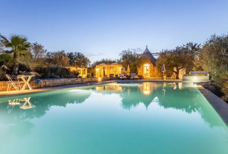 Masseria in pietra con piscina illuminata al crepuscolo tra gli ulivi del Salento